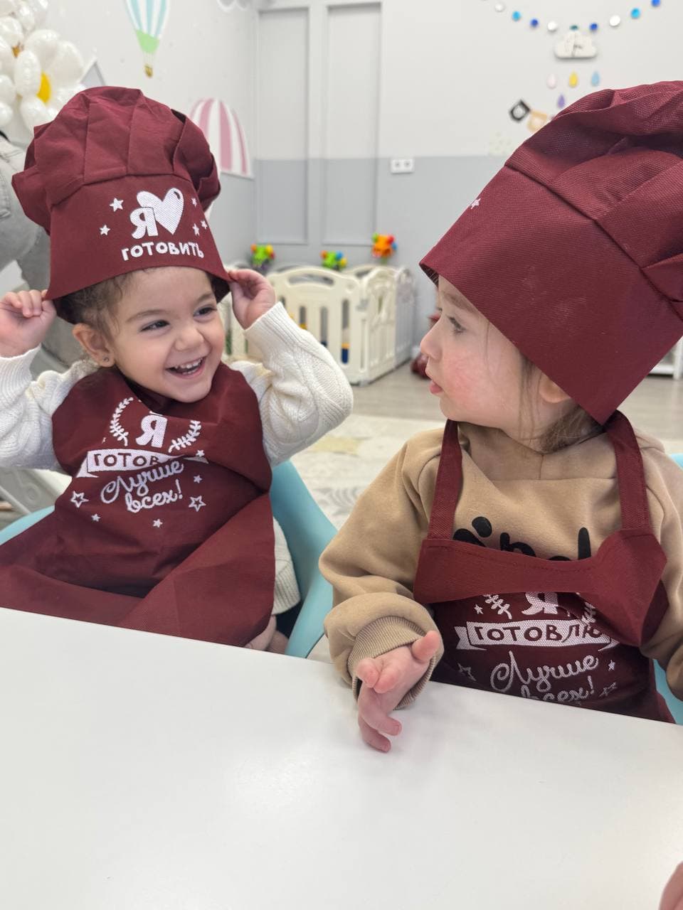 Дети в поварских фартуках улыбаются за столом